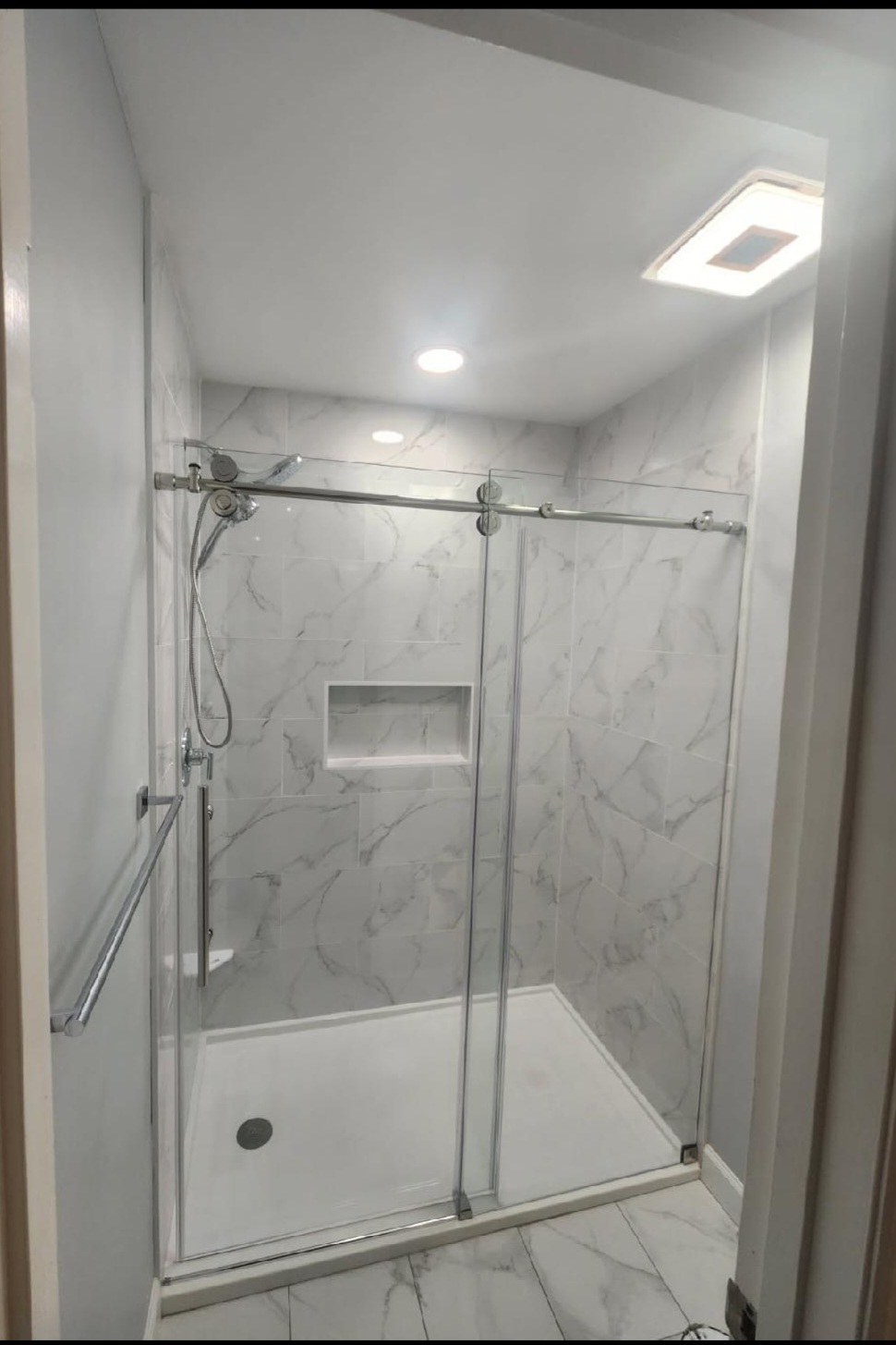 A crisp white marble-look shower with a recessed niche, subway-set walls and a frameless sliding-glass door.