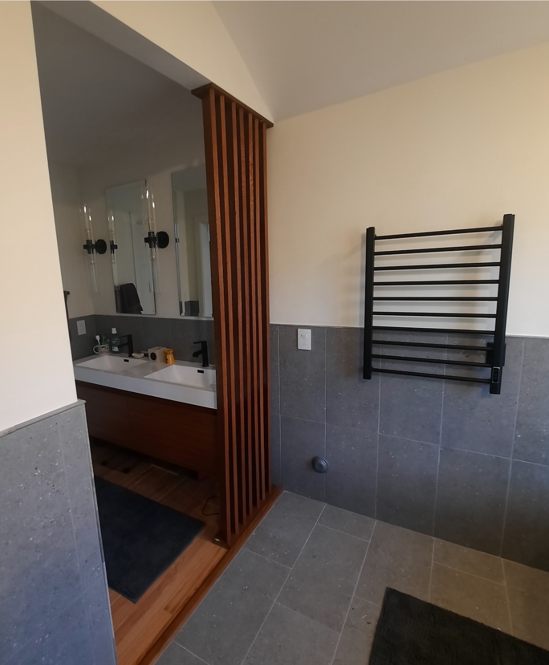 A contemporary master bathroom with a floating wood double vanity, slate-tile wainscot, a wood slat divider and a heated towel rack.