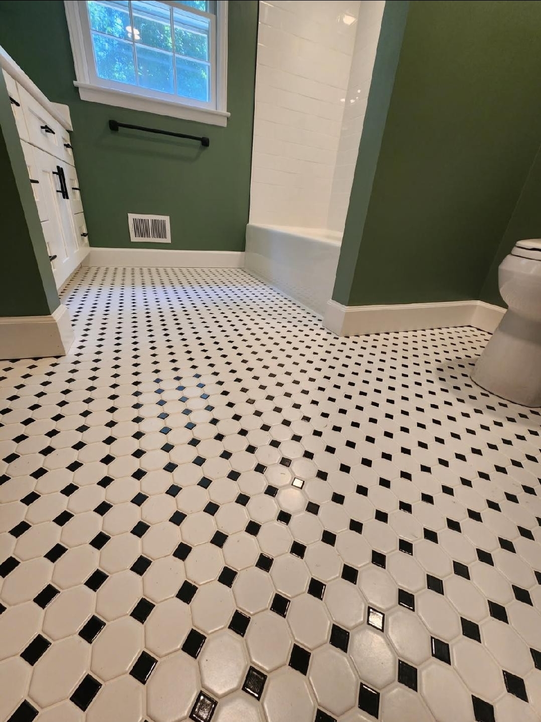 A classic black-and-white octagon mosaic tile floor laid against deep green walls — the finishing detail on a period-style bath.